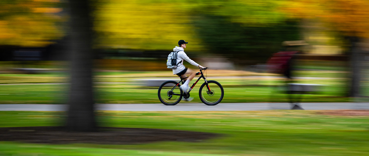 A student cruises across campus on a bike amid fall colors