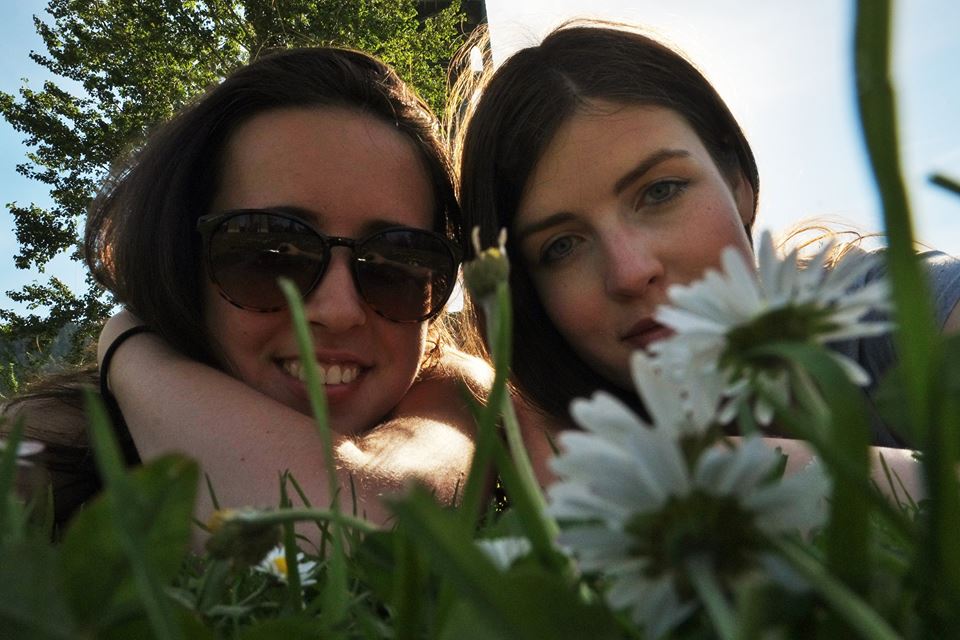 Two female students smiling with a flower on a sunny day