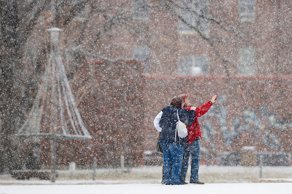 two students take a picture while snow falls on campus