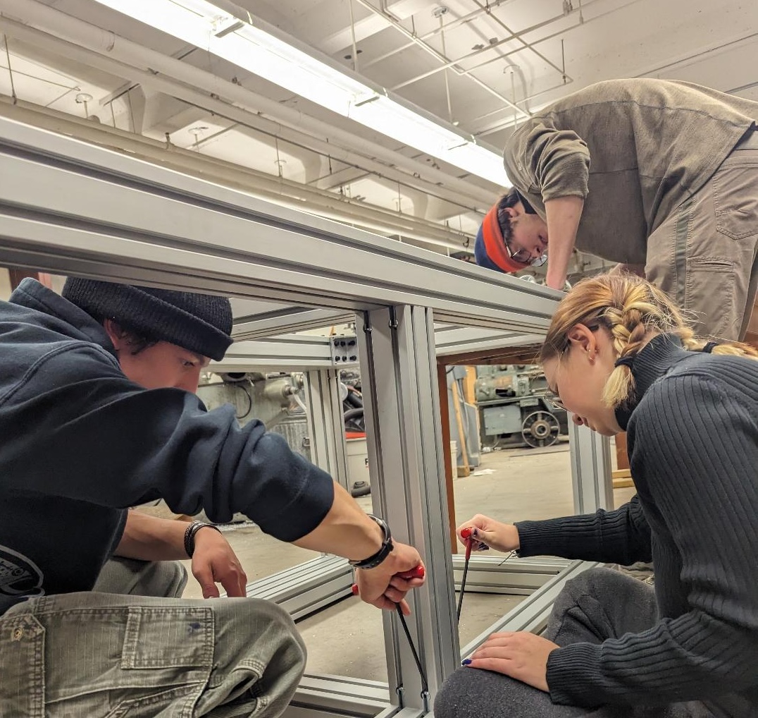 Three students build metal frame.