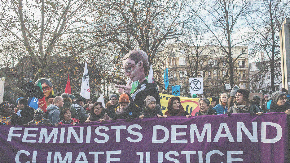 people marching in protest holding a banner that reads "feminists demand climate justice."