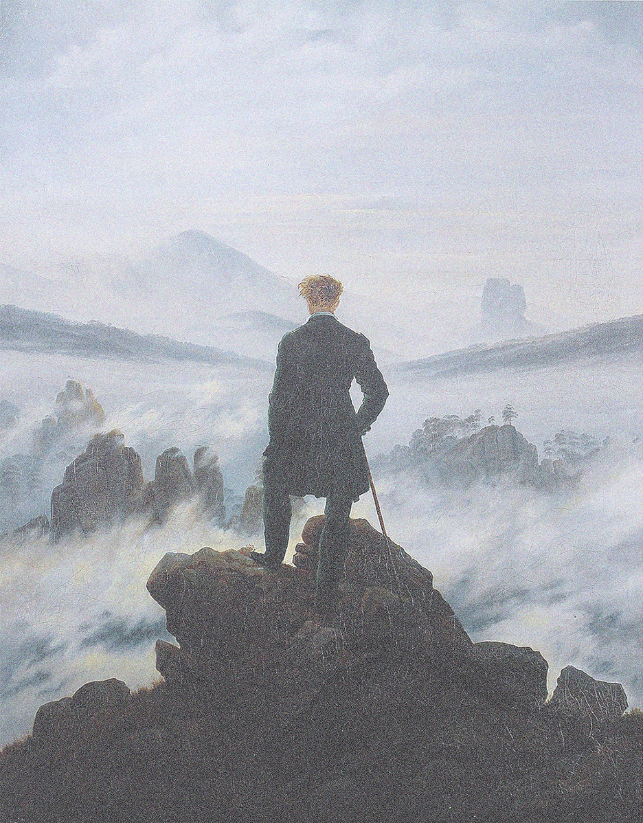 man standing at mountain peak looking out over the clouds and into the distance